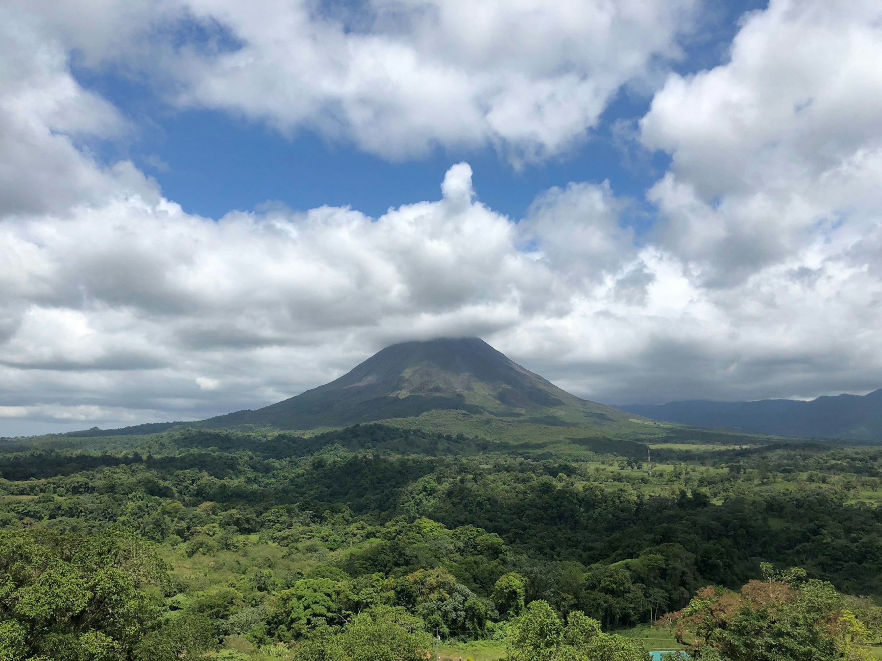 Arenal volcano rising over green forest, its peak wrapped in a band of cloud.
