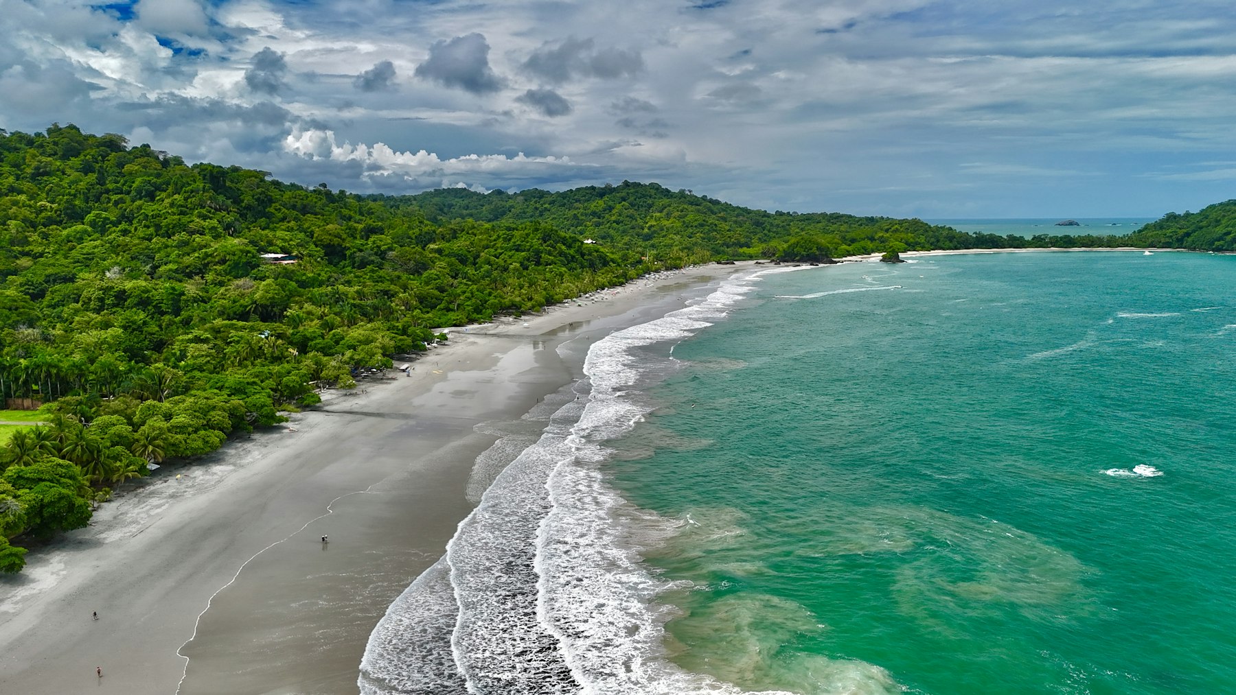 Aerial view of a pale beach, turquoise surf, and forested headlands at Manuel Antonio.